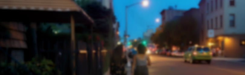 Image description: A blurry image of two women walking along the street. The photo is taken from behind.